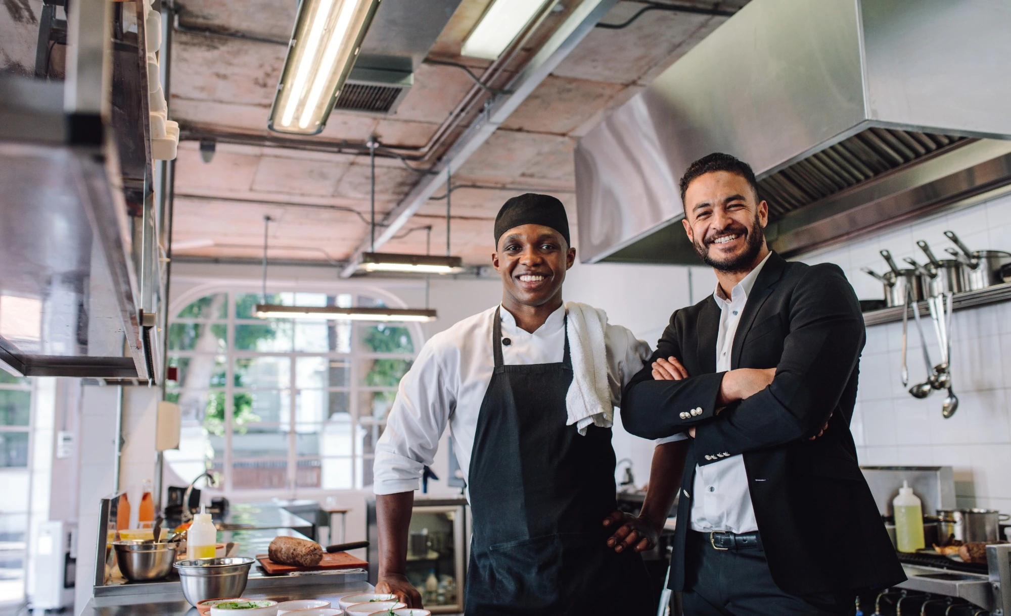A chef and a restaurant owner smiling in their kitchen